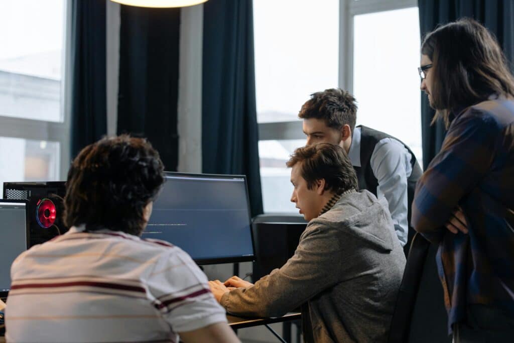 Four men gathered around a computer monitor in an office, looking at the screen