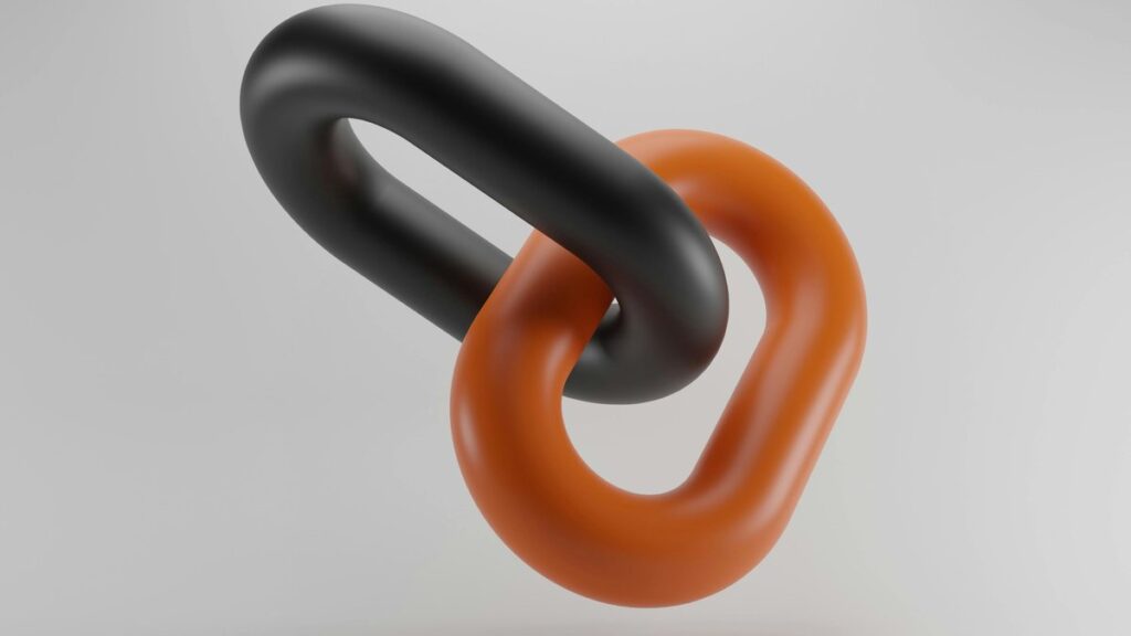 Two interlocked chain links, one black and one orange, on a light grey background